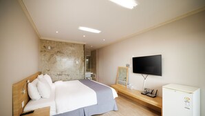 A hotel room with a bed, a television, a refrigerator, and a wooden bench. - Pension Yeoli (Seogwipo)