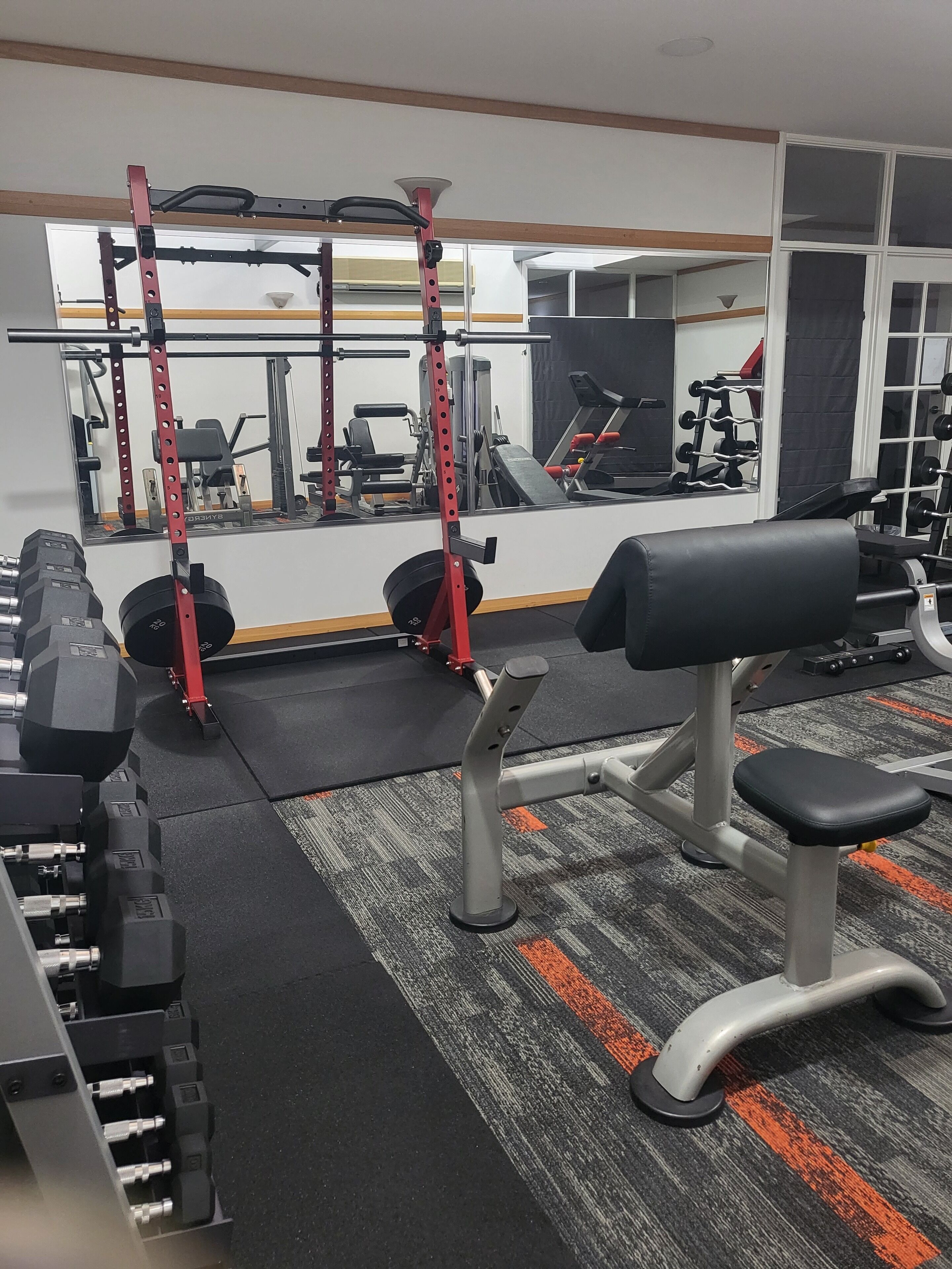 Un gimnasio con equipo de levantamiento de pesas, bancos y un espejo.