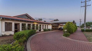 A row of modern, single-story buildings with a red-tiled roof, a paved walkway, and well-maintained landscaping. - Banksia Motel Collie (Collie)