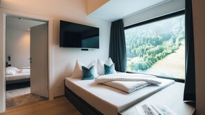 A modern bedroom with a large window, a flat-screen TV, and a bed with pillows.