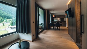A modern hotel room with a large window, a dining area, and a kitchen.