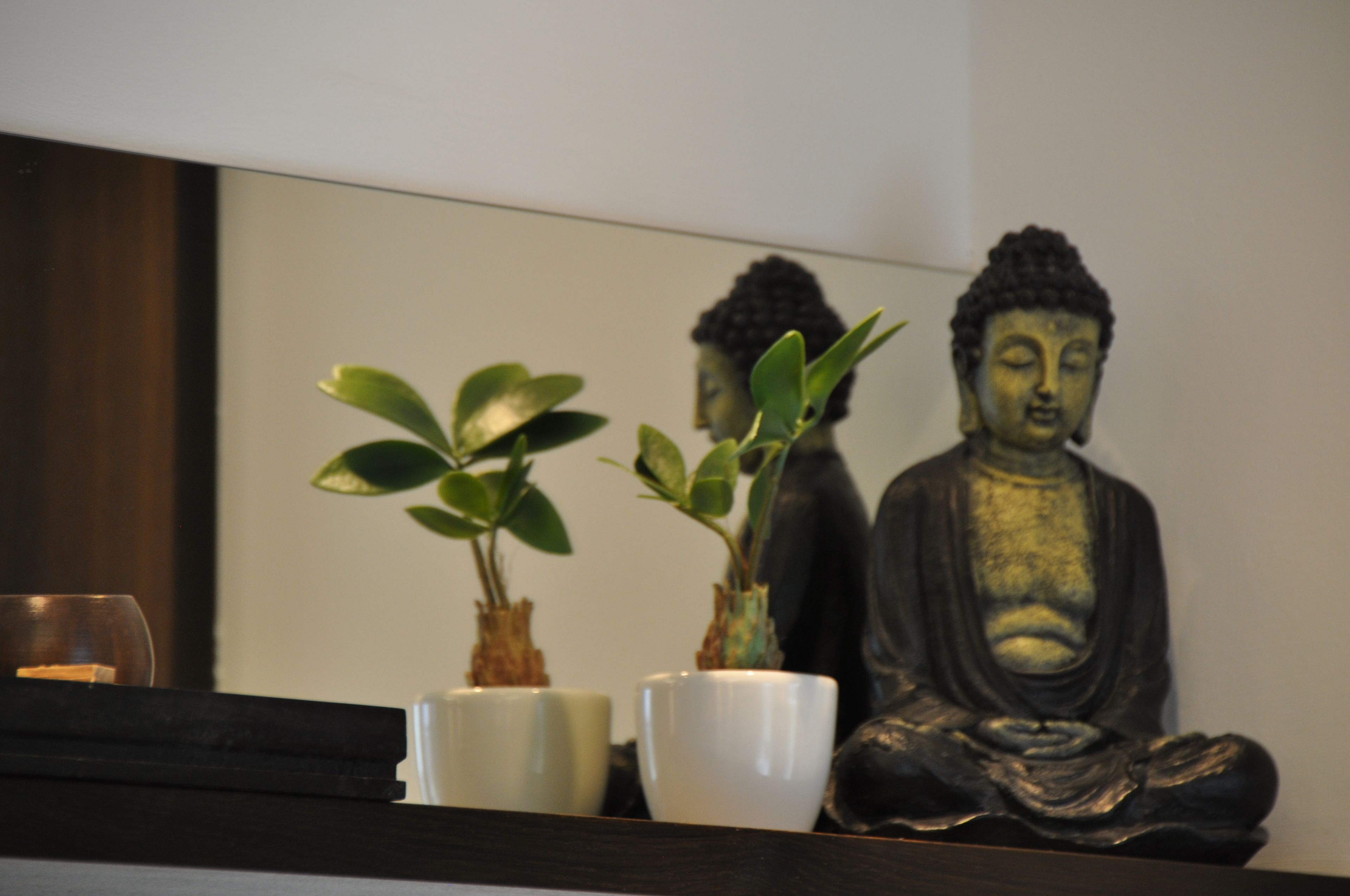 A statue of Buddha, two potted plants, and a white cup on a shelf.