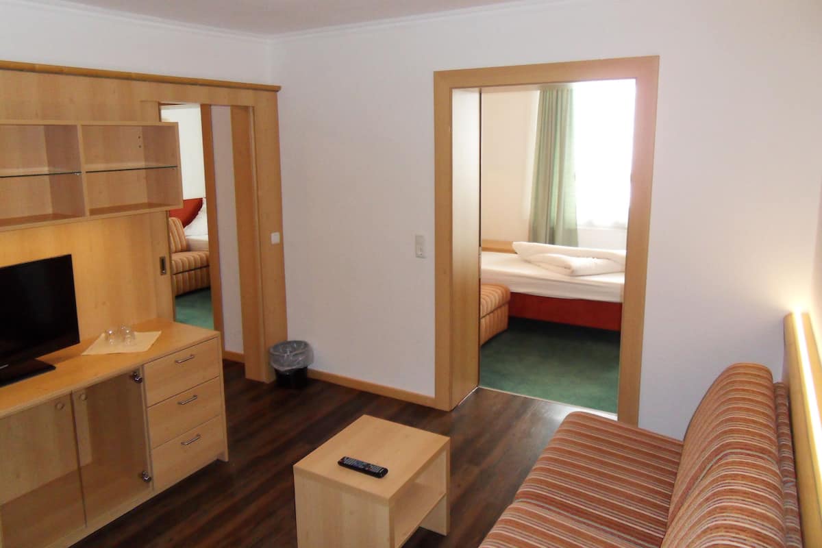 A compact hotel room with a wooden desk, a television, a single bed, and a sofa.