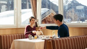 A dining area with a table set for breakfast, a bench, and a view of snow-covered mountains through large windows.