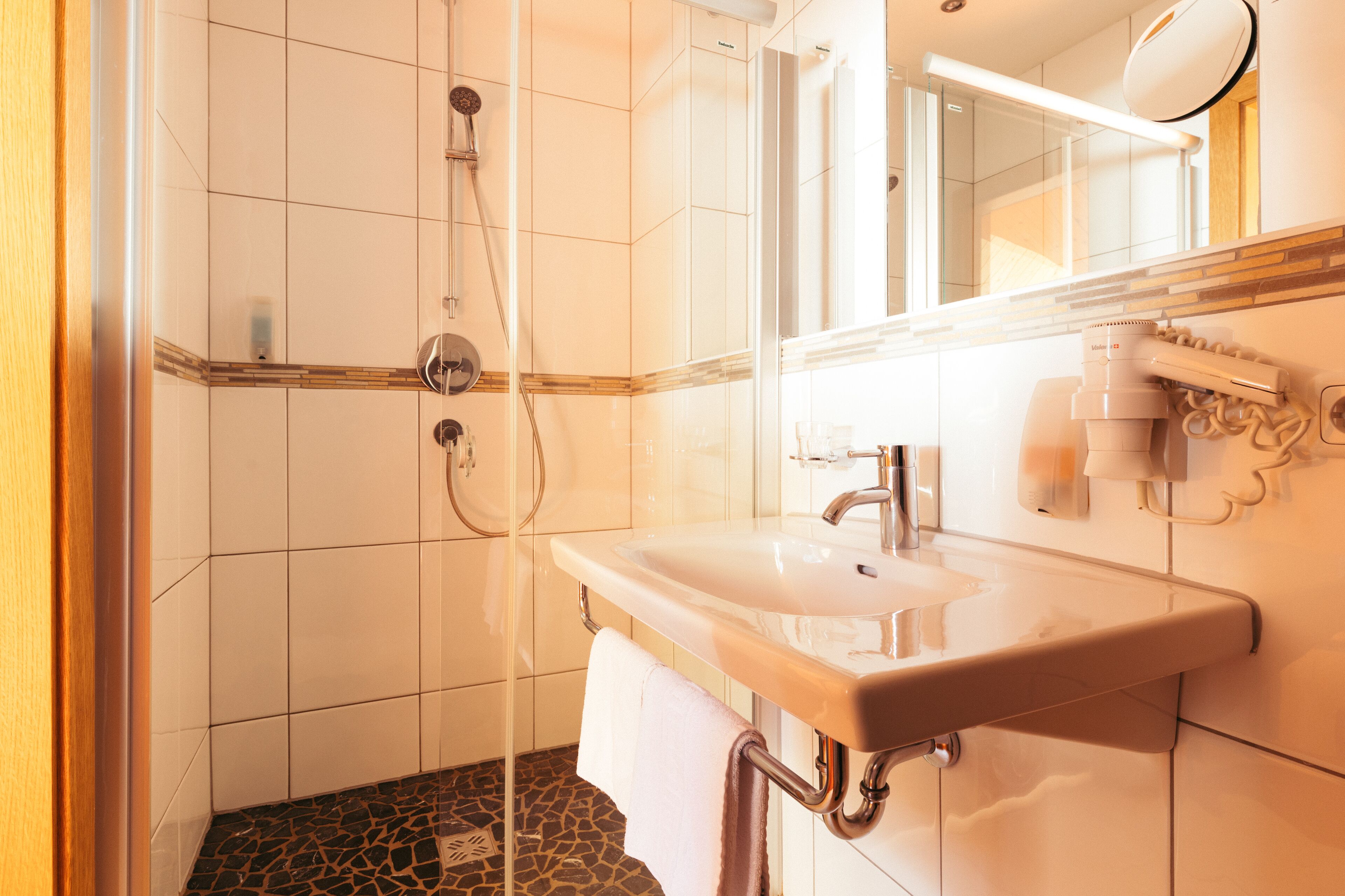 A bathroom with a white sink, a mirror, a shower, and a towel rack.