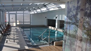 A large indoor swimming pool with a glass wall, wooden deck, and a mural of trees.