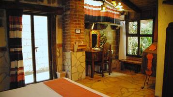 A room with a bed, a table with chairs, a window with curtains, and a stone wall.