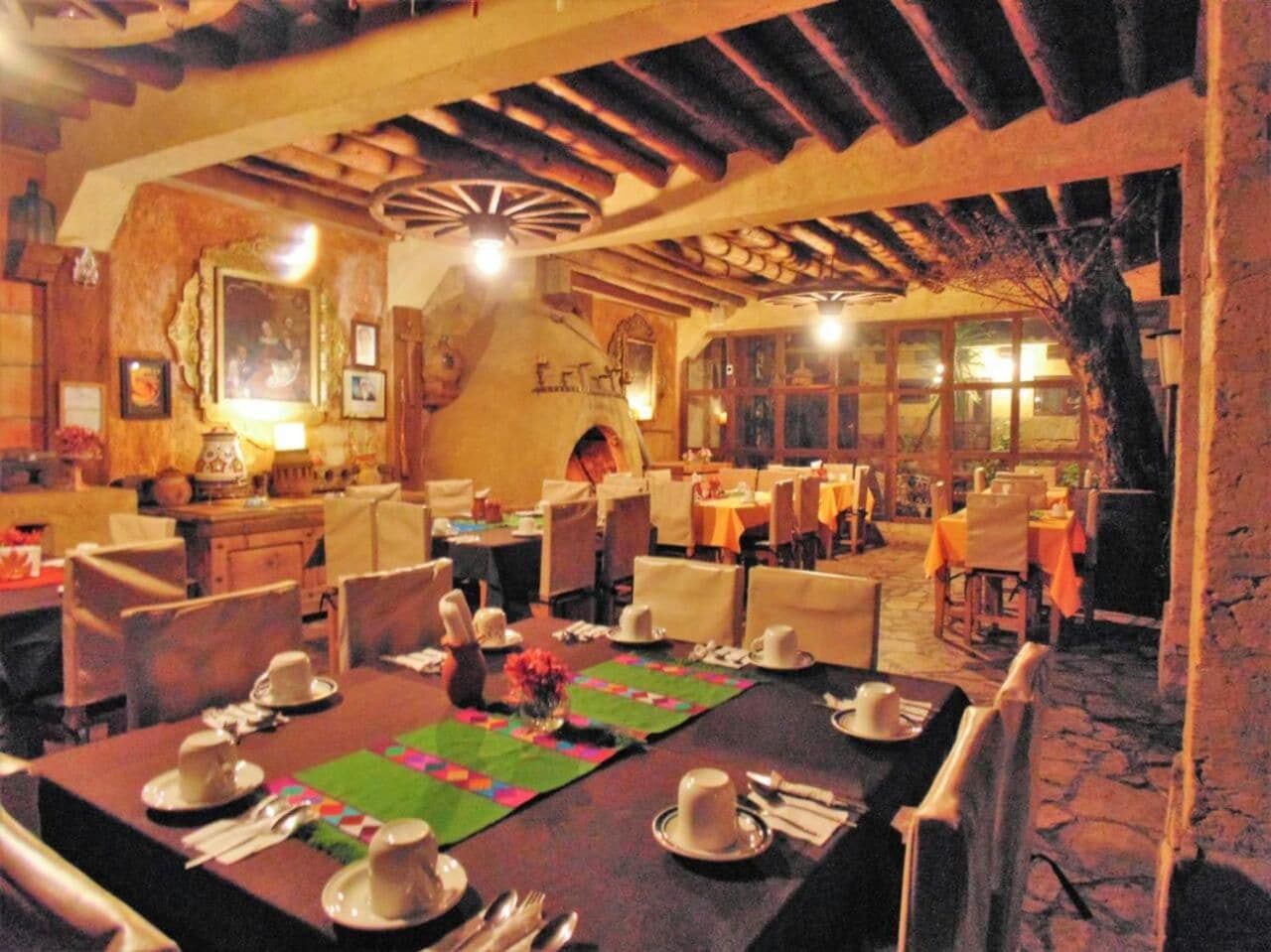 Un restaurant amb taules preparades per dinar, sostre de fusta i interior rústic.