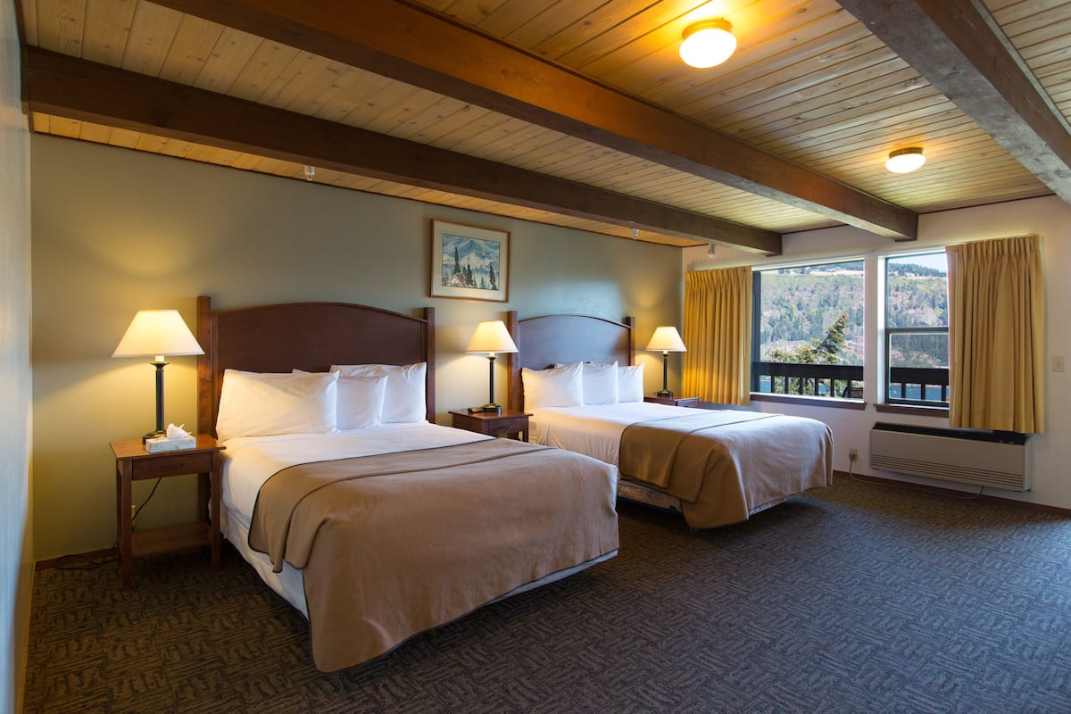 A hotel room with two beds, wooden headboards, and a large window with a view of the mountains.