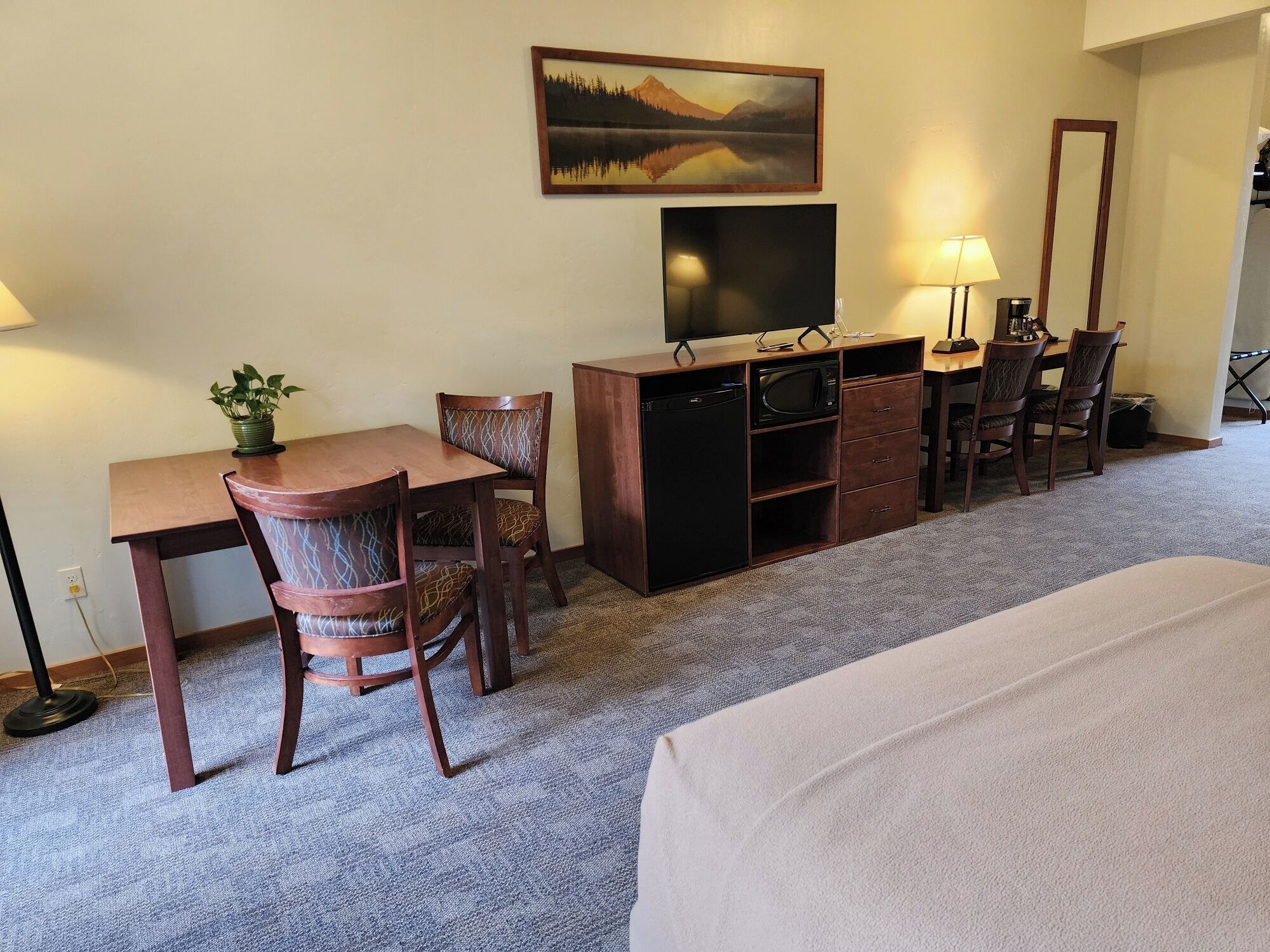 Quarto de hotel com cama, escrivaninha, cadeira, televisão, cómoda e abajur.