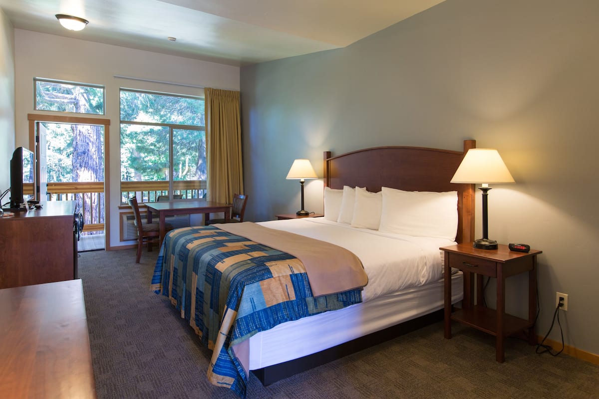 A hotel room with a large bed, two bedside lamps, a wooden nightstand, a desk with a chair, and a window with curtains.