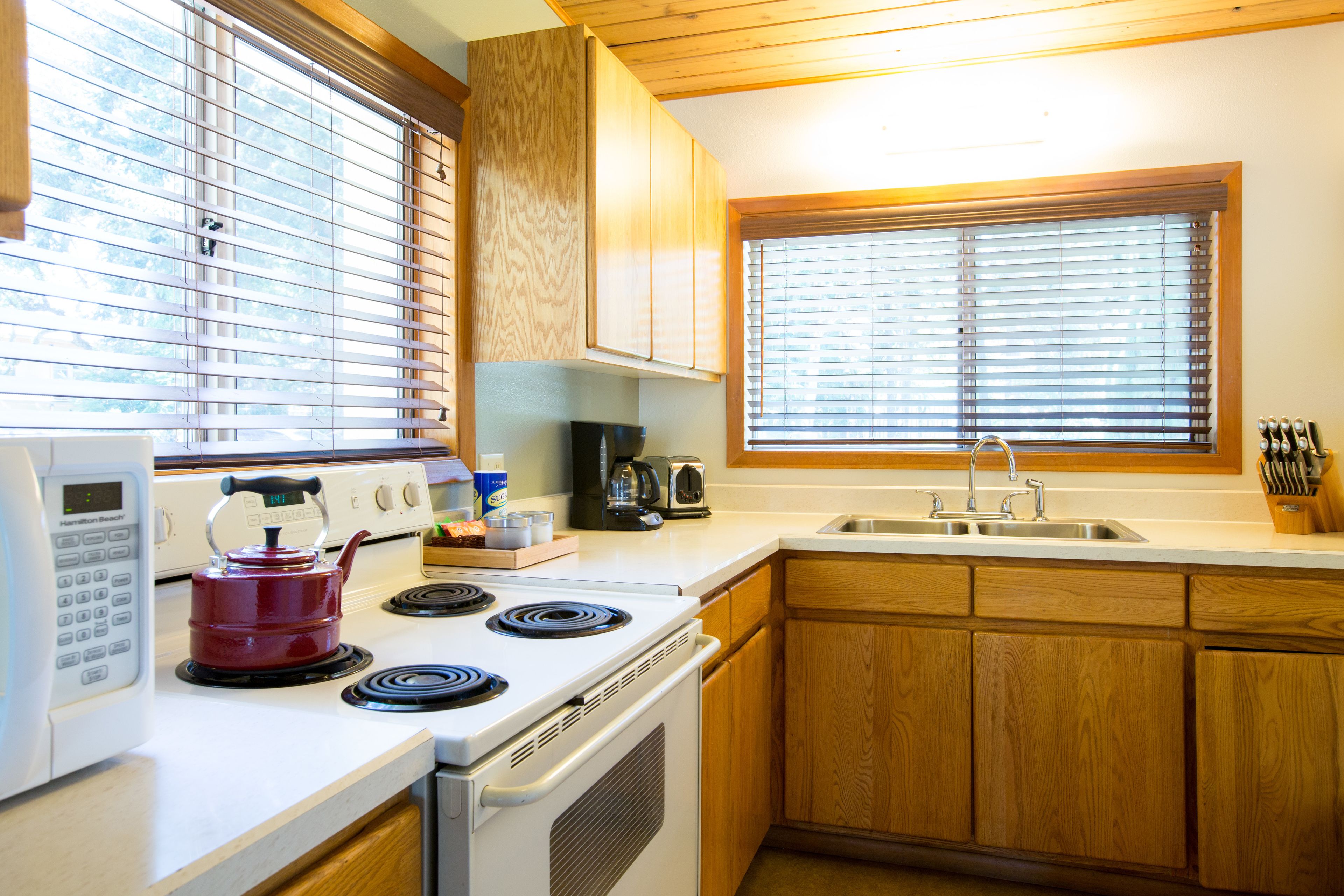 Une cuisine avec des meubles de rangement en bois, une cuisinière, un four à micro-ondes et une fenêtre avec des stores.