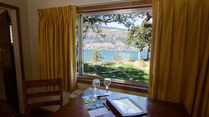 Una mesa de comedor con vistas a un lago y colinas, cortinas amarillas y un cuadro enmarcado.