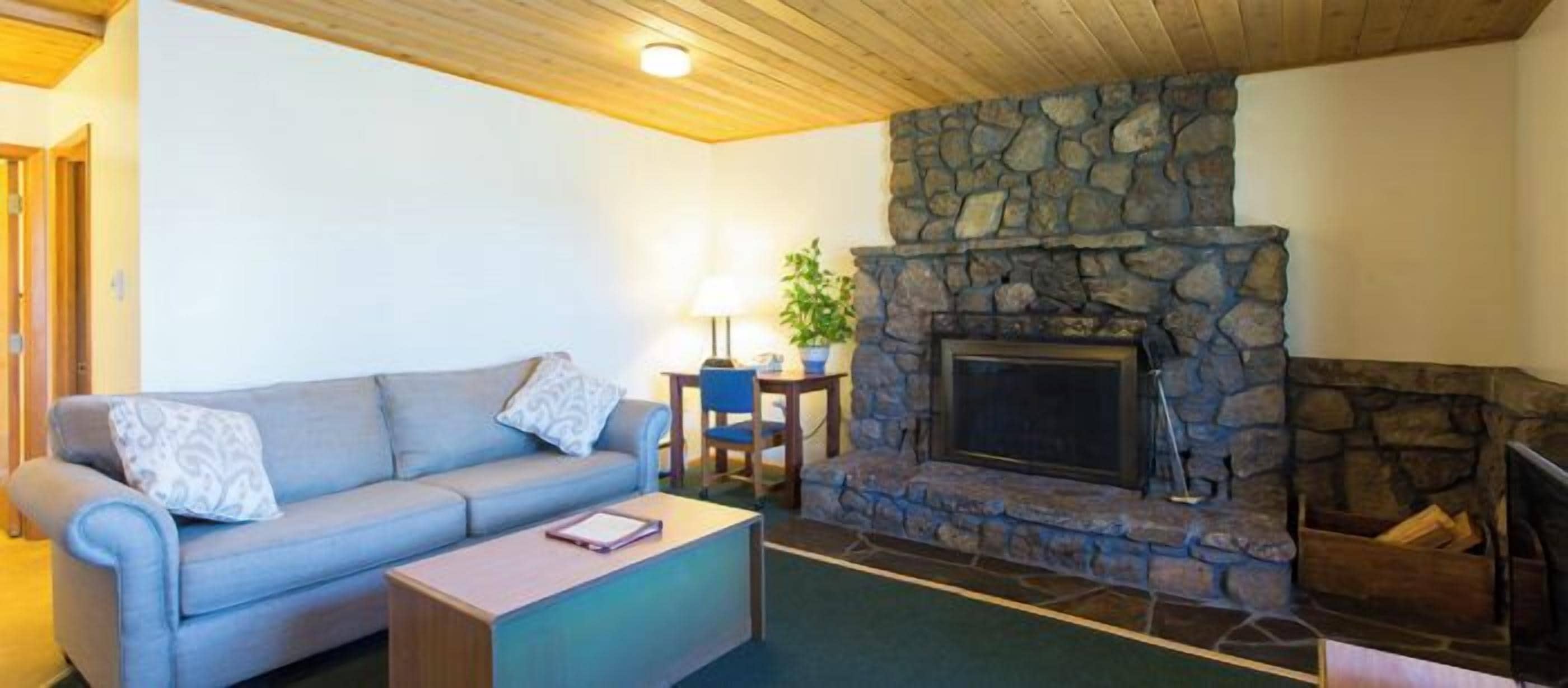 A cozy living room with a stone fireplace, a blue sofa, and a small table with a lamp.