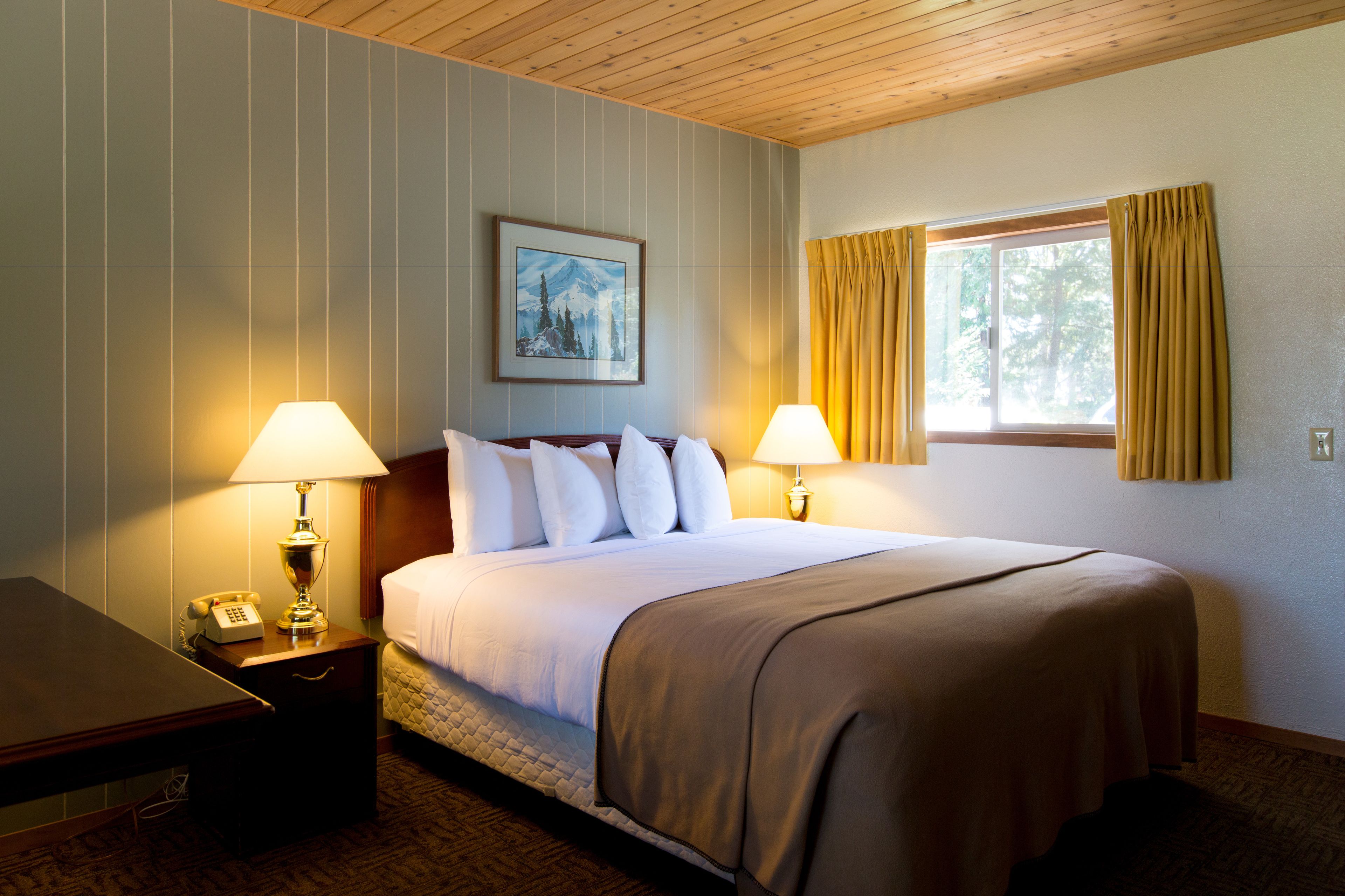 A hotel room with a large bed, two bedside lamps, a painting on the wall, and a window with curtains.