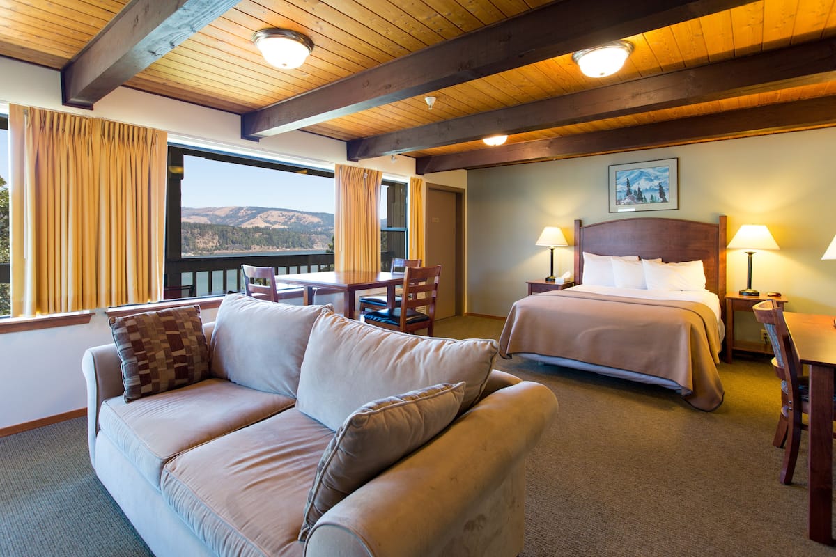 A hotel room with a large bed, a sofa, a dining table, and a view of the mountains.