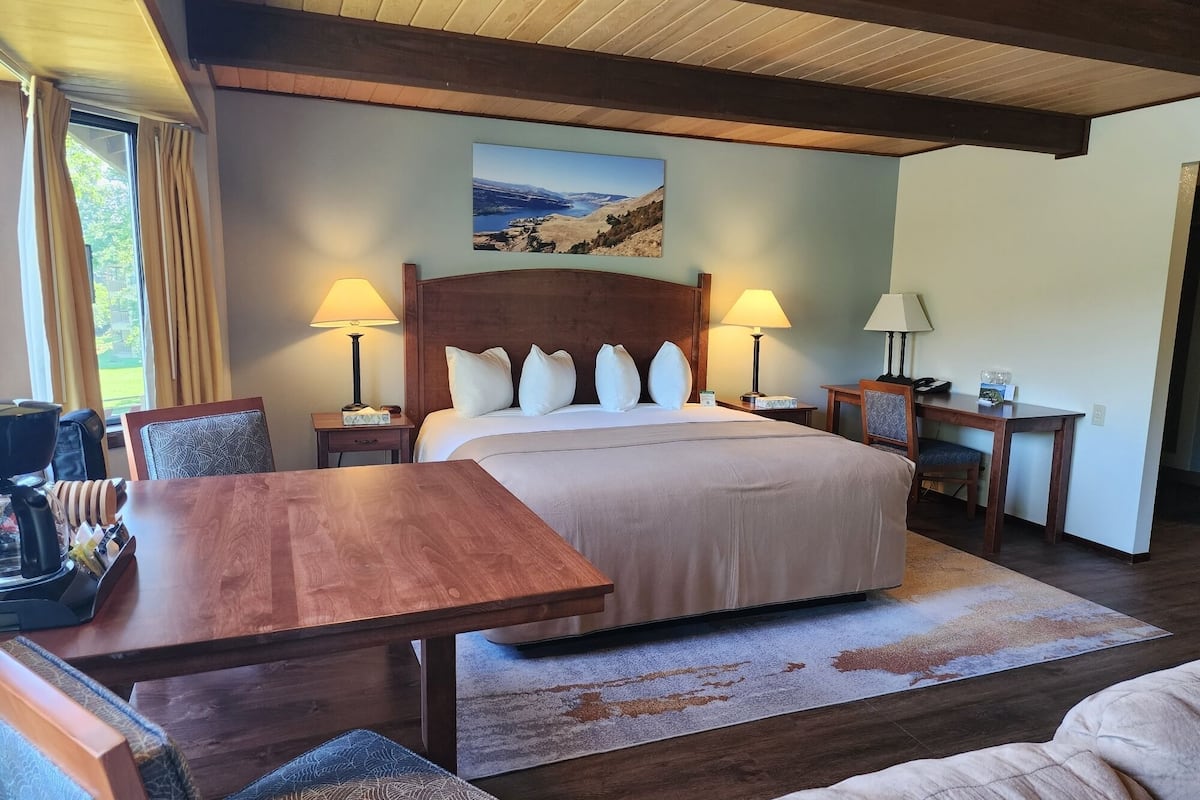 A well-lit room with a large bed, two bedside lamps, a wooden table, and a desk with a chair.