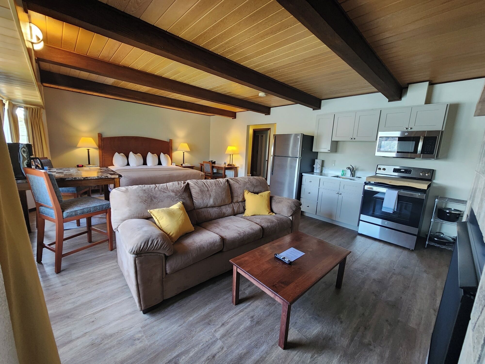 A hotel room with a sofa, a coffee table, a bed, a desk, and a kitchenette.
