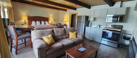 A hotel room with a sofa, a coffee table, a bed, a desk, and a kitchenette.