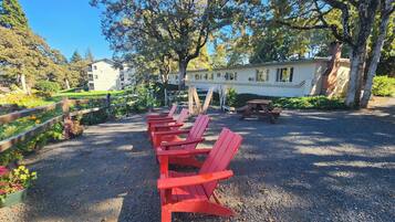 A gravel area with red Adirondack chairs and a picnic table, surrounded by trees and a building with a white exterior.