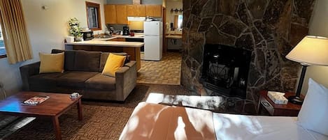 A hotel room with a large bed, a sofa, a coffee table, and a stone accent wall.