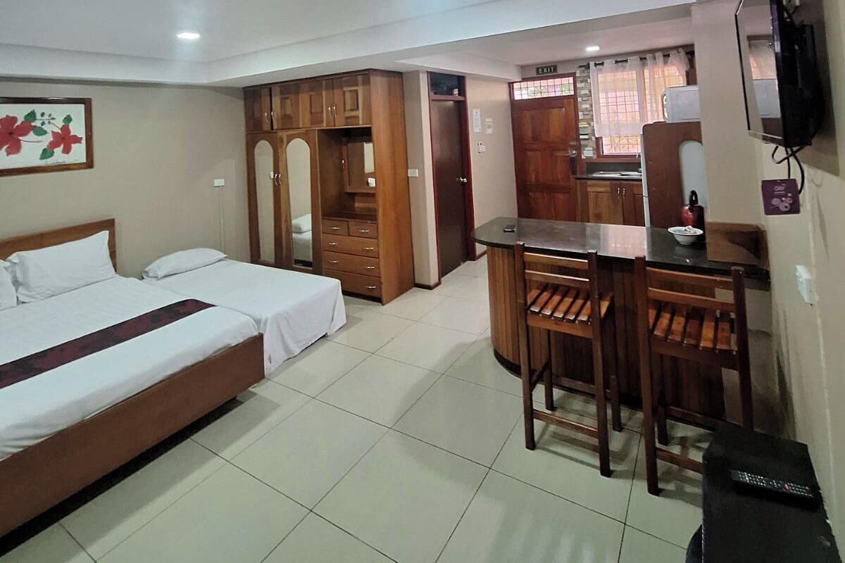 A hotel room with a bed, a desk, and a chair. There is a TV mounted on the wall and a window with curtains.