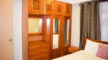 Un dormitorio con un armario de madera, una cama con almohadas y una mesita de noche.