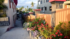 A narrow alleyway with a row of colorful flowers on the right, leading to a building with a red roof. - Al-Minhaj Service Apartments (Nadi)