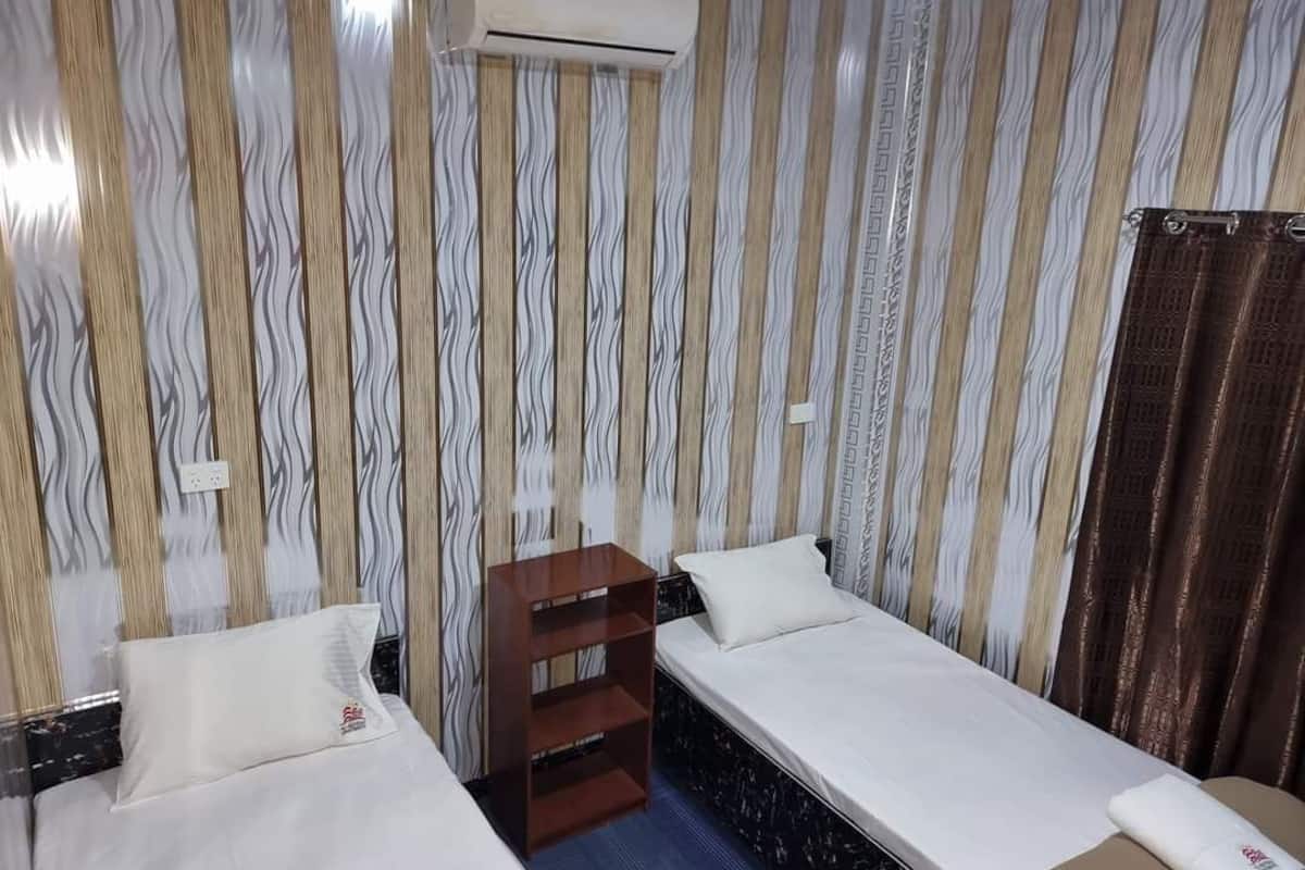 A hotel room with two single beds, a wooden nightstand, an air conditioning unit, and striped wallpaper.