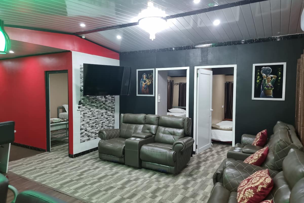 A room with a sofa, a reclining chair, a flat-screen TV, a patterned wall, and a door leading to another room.