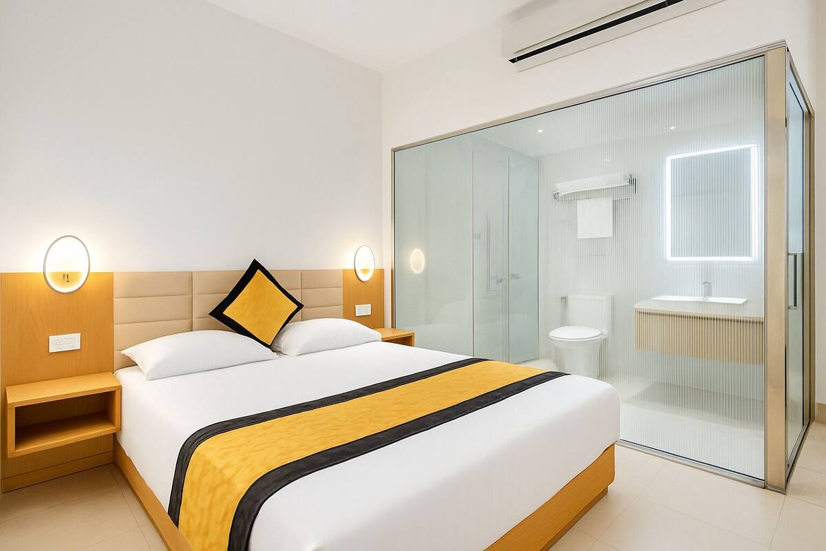 Une chambre d’hôtel moderne dotée d’un grand lit, de tables de chevet, d’une douche séparée par une paroi de verre et d’une salle de bain visible.