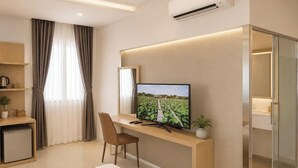 A modern hotel room with a flat-screen TV, a desk, a chair, a small fridge, a bedside table with a lamp, and a large window with curtains. - S79 Residences La Rose Spa (Ho Chi Minh City)