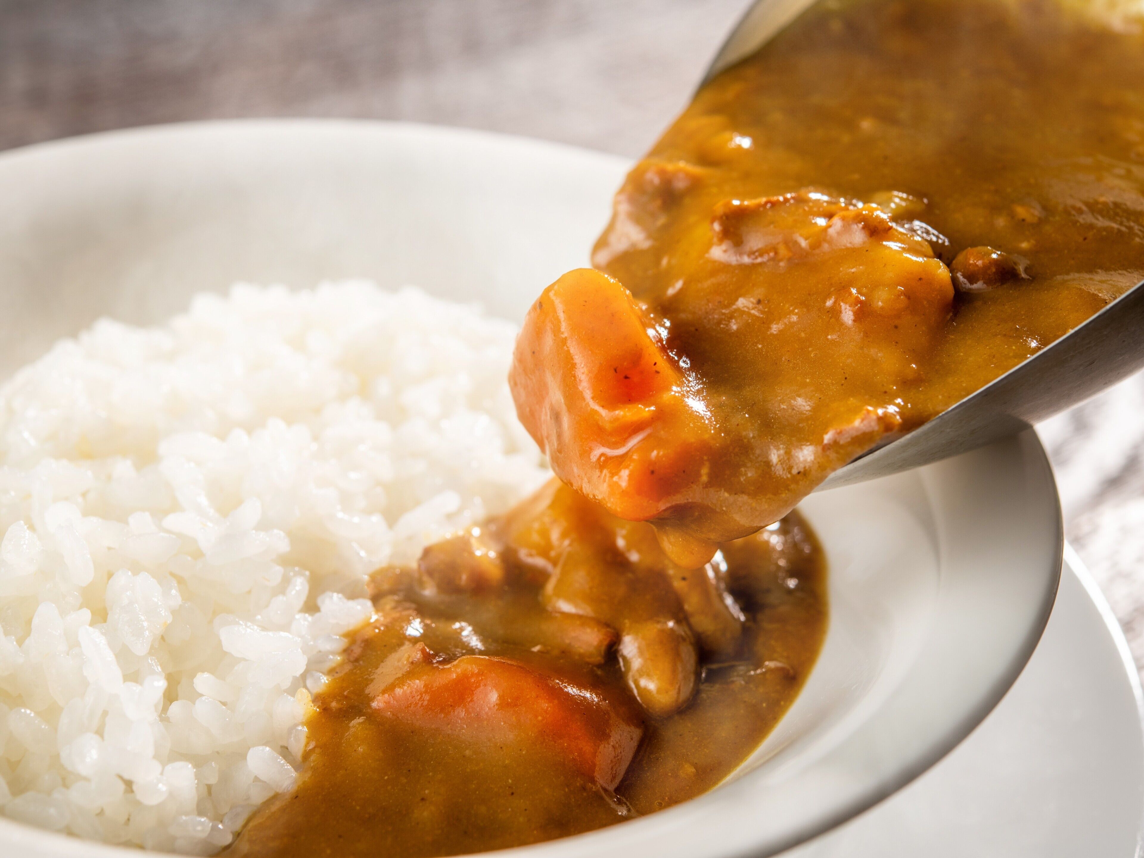 A bowl of white rice with a spoonful of curry containing meat and vegetables.