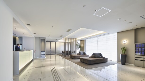 A modern lobby with a reception desk, seating area, and a large window providing natural light.