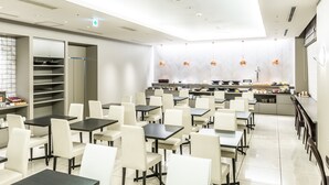 A modern restaurant with a clean, minimalist interior, featuring white and black tables and chairs, a central kitchen area, and a bright, well-lit ambiance.
