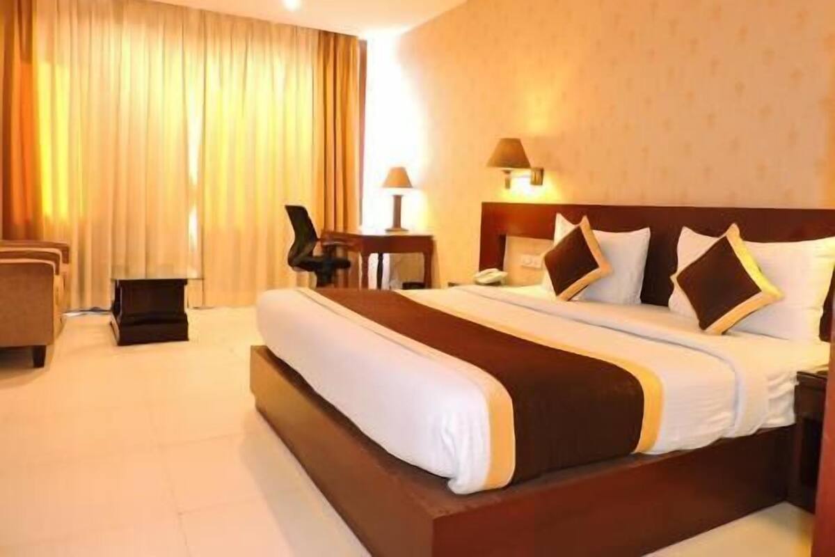 A hotel room with a large bed, a desk with a chair, a lamp, and a view of the outdoors.