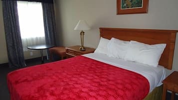 A hotel room with a large bed, a nightstand, a lamp, a small table, and a painting on the wall.