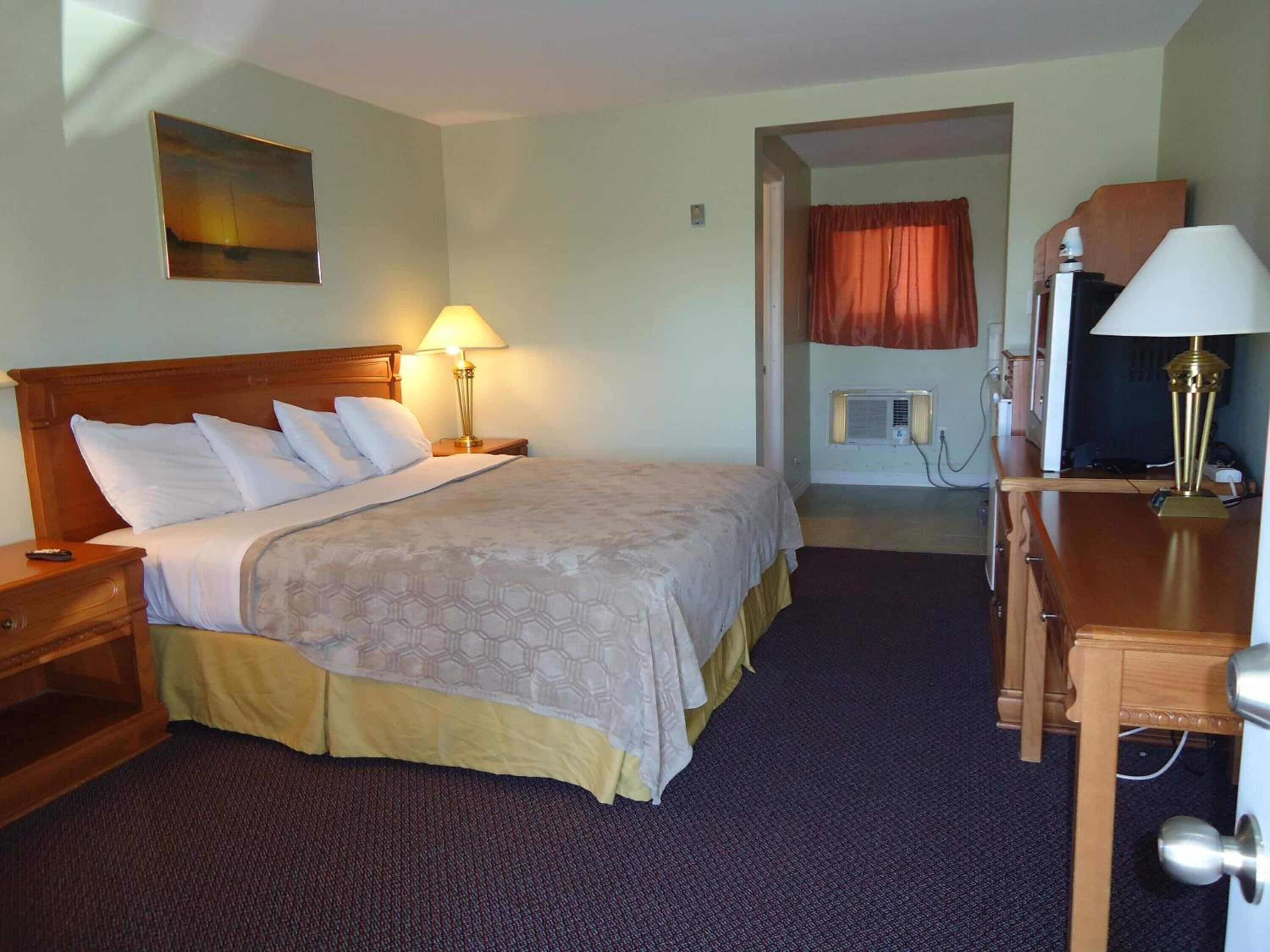 A hotel room with a bed, bedside lamps, a desk, and a television.