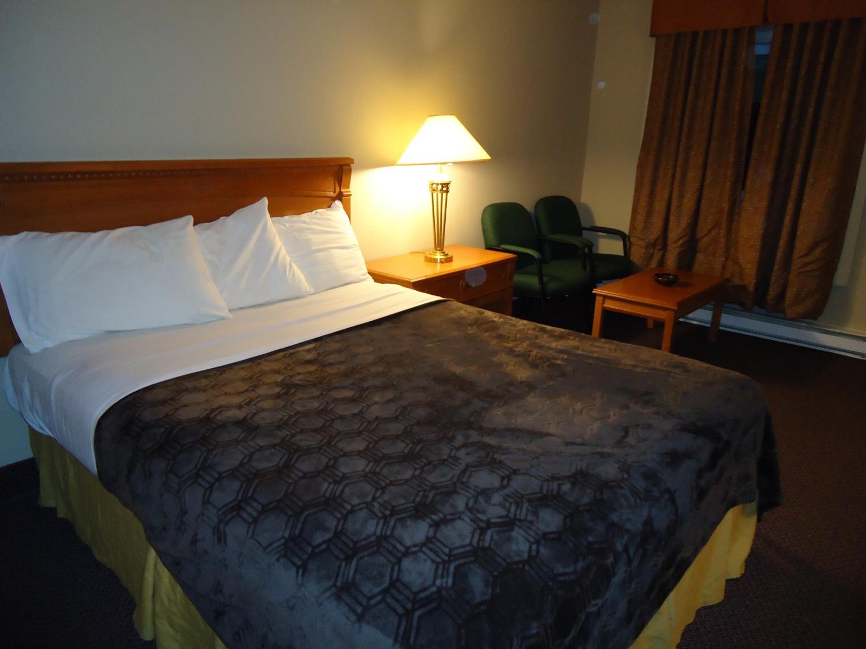 Una habitación de hotel con una cama grande, una mesita de noche con lámpara, dos sillas y una pequeña mesa.