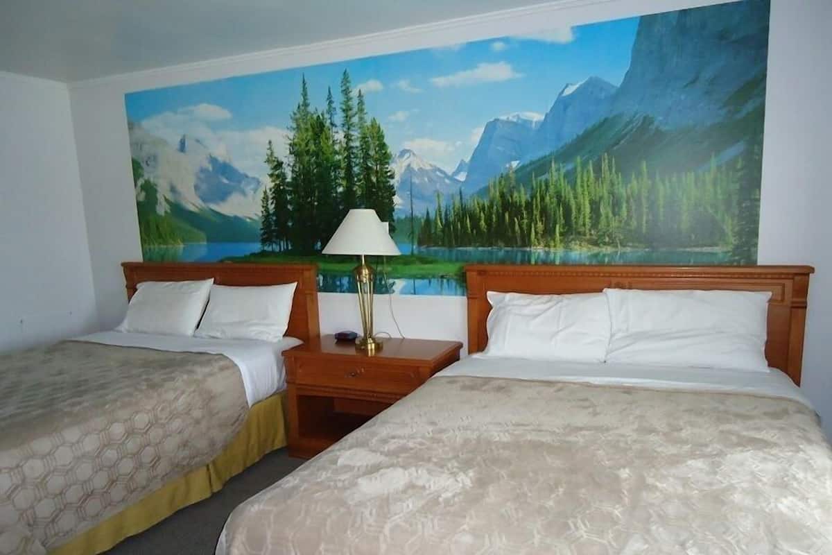 A hotel room with two beds, a nightstand with a lamp, and a large mural of a mountain landscape.