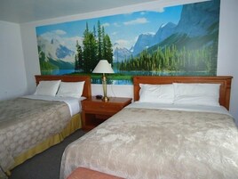 Habitación de hotel con dos camas, una mesita de noche con lámpara y un gran mural de un paisaje montañoso.