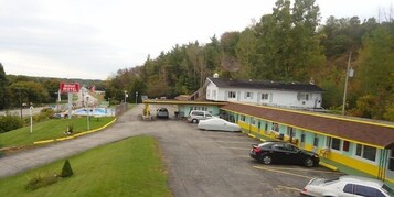 Un motel con estacionamiento, piscina y un edificio de fachada amarilla y blanca.