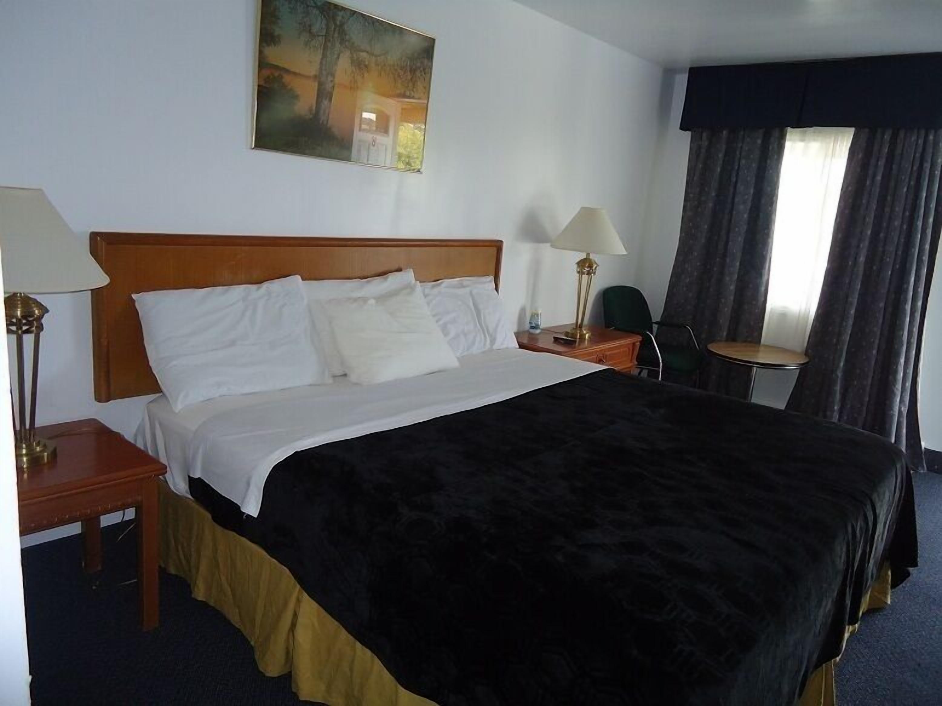 A hotel room with a large bed, two bedside tables with lamps, a small round table, a chair, and a painting on the wall.