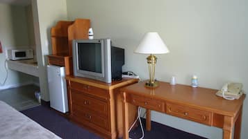 Una habitación de hotel con cama, escritorio de madera, televisor, lámpara, microondas, refrigerador y teléfono.