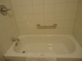 Una bañera blanca estándar con una barra de apoyo, un grifo y un dispensador de jabón.