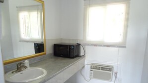 A bathroom with a sink, mirror, black microwave, and window with blinds. - Westmount Motel (South-West Oxford)