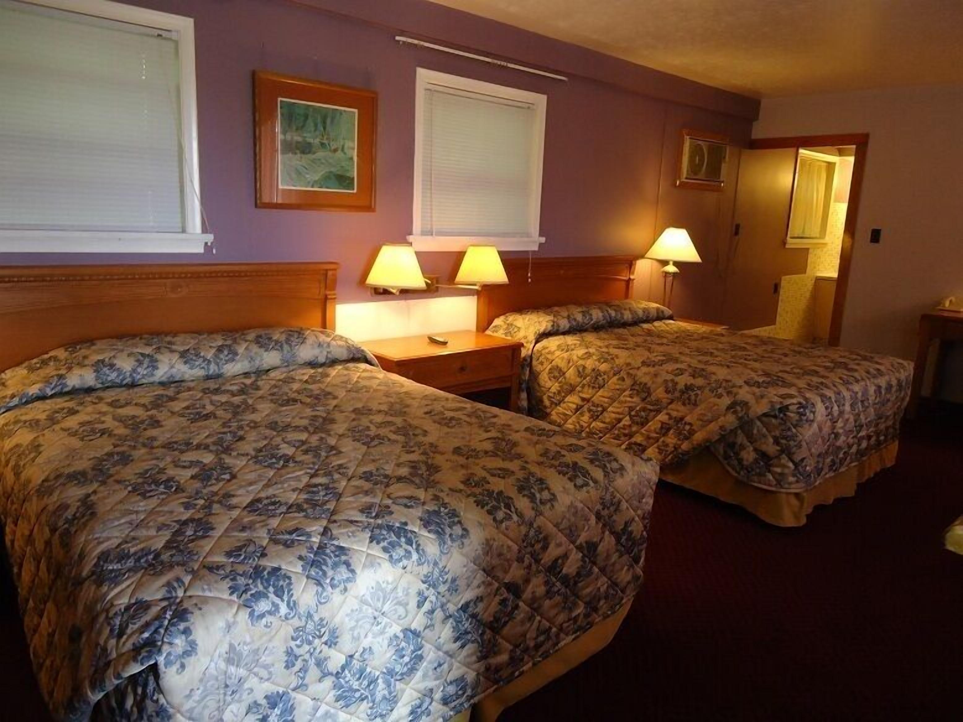 A hotel room with two beds, each with floral bedding, a wooden headboard, bedside lamps, and a framed picture on the wall.