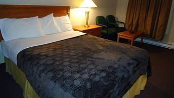 A hotel room with a large bed, a nightstand, a lamp, a chair, and a window with curtains.