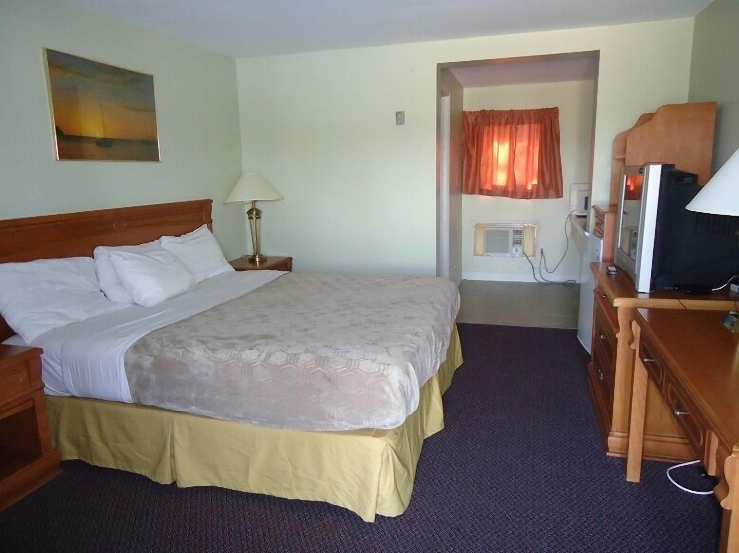 A hotel room with a bed, a desk, a lamp, a television, and a painting on the wall.