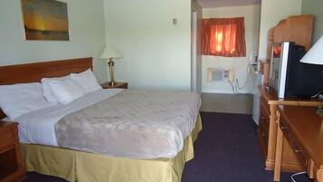 A hotel room with a bed, a desk, a lamp, a television, and a painting on the wall.